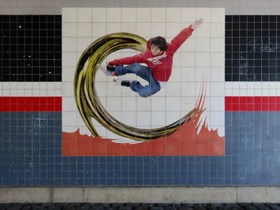 912846 Afbeelding van een tegelplateau met een afbeelding van een jonge skater op een golf, in de oostelijke muur van ...